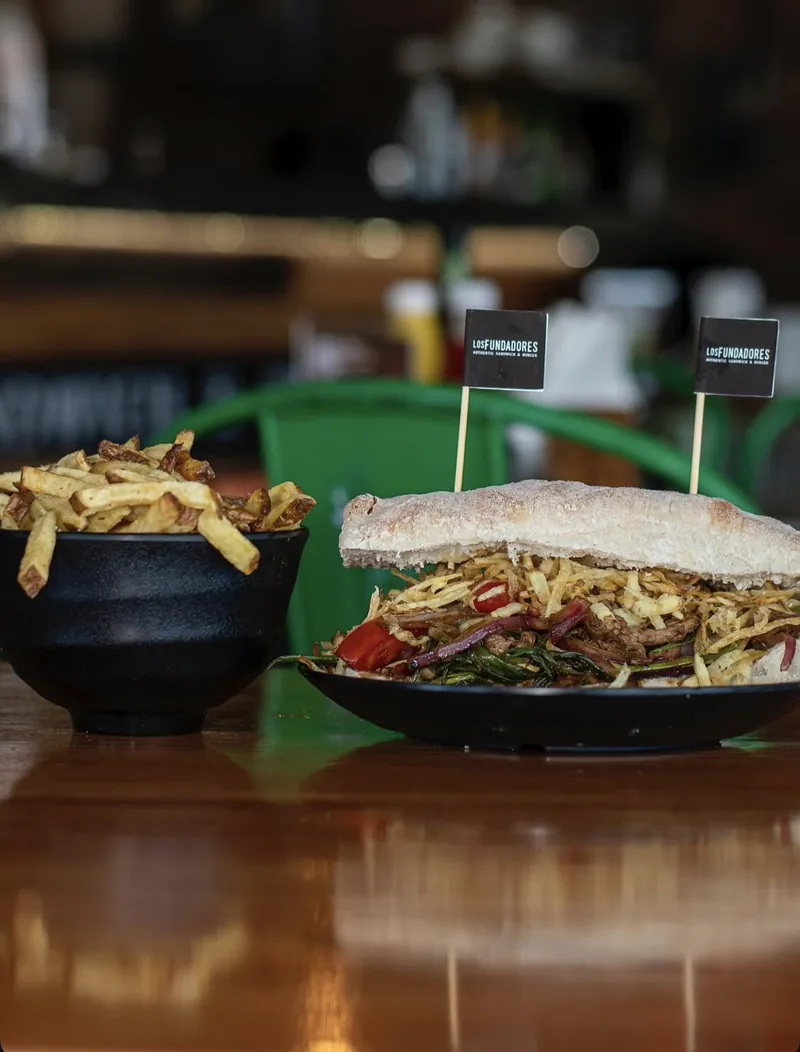 Sándwich Lomo Saltado con papas hilo, junto a un bowl de papas fritas