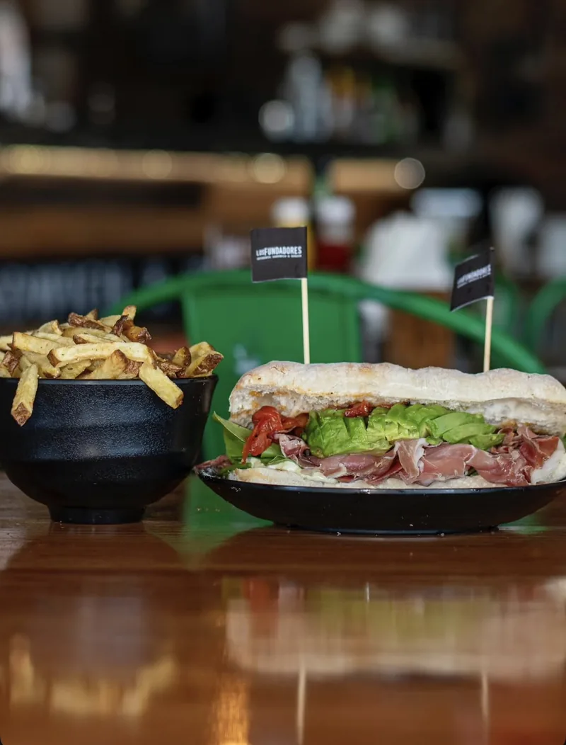 Sándwich Mediterráneo con jamón serrano y palta, junto a un bowl de papas fritas