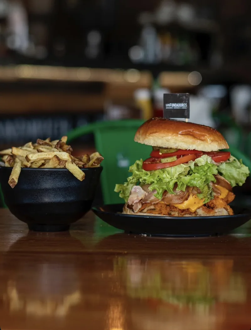 Milanesa con lechuga, tomate, tocino y queso cheddar, junto a un bowl de papas fritas
